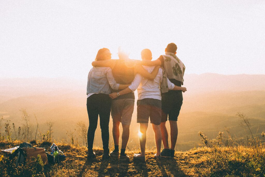 group of friends having quality time together standing arm in arm on a hill top in the golden light of sunset