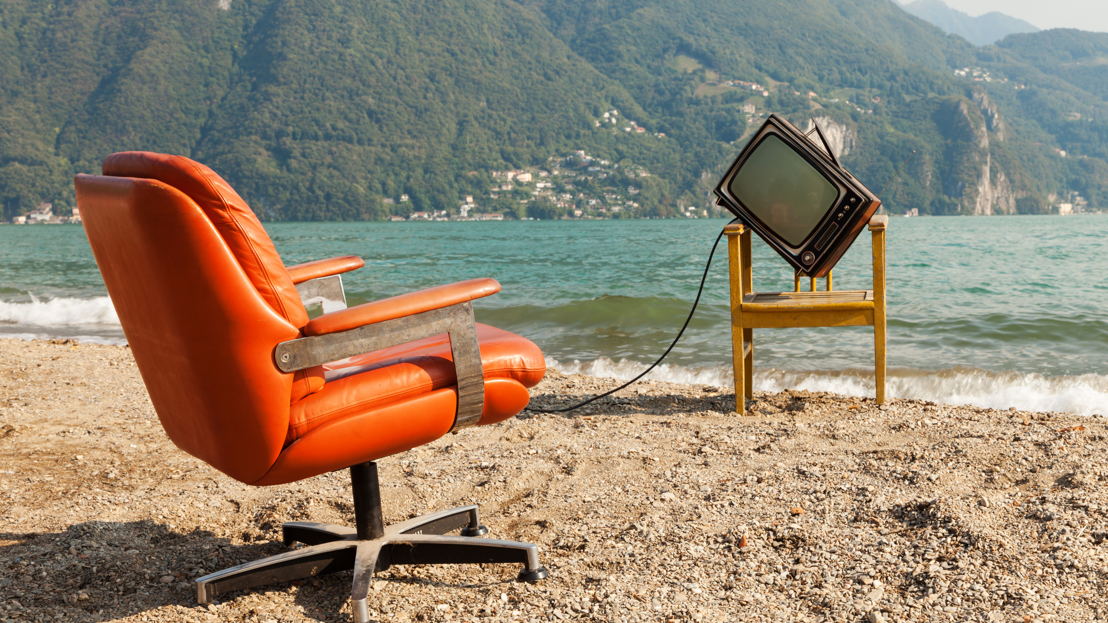 quirky image of bright orange chair on a beach with a vintage television